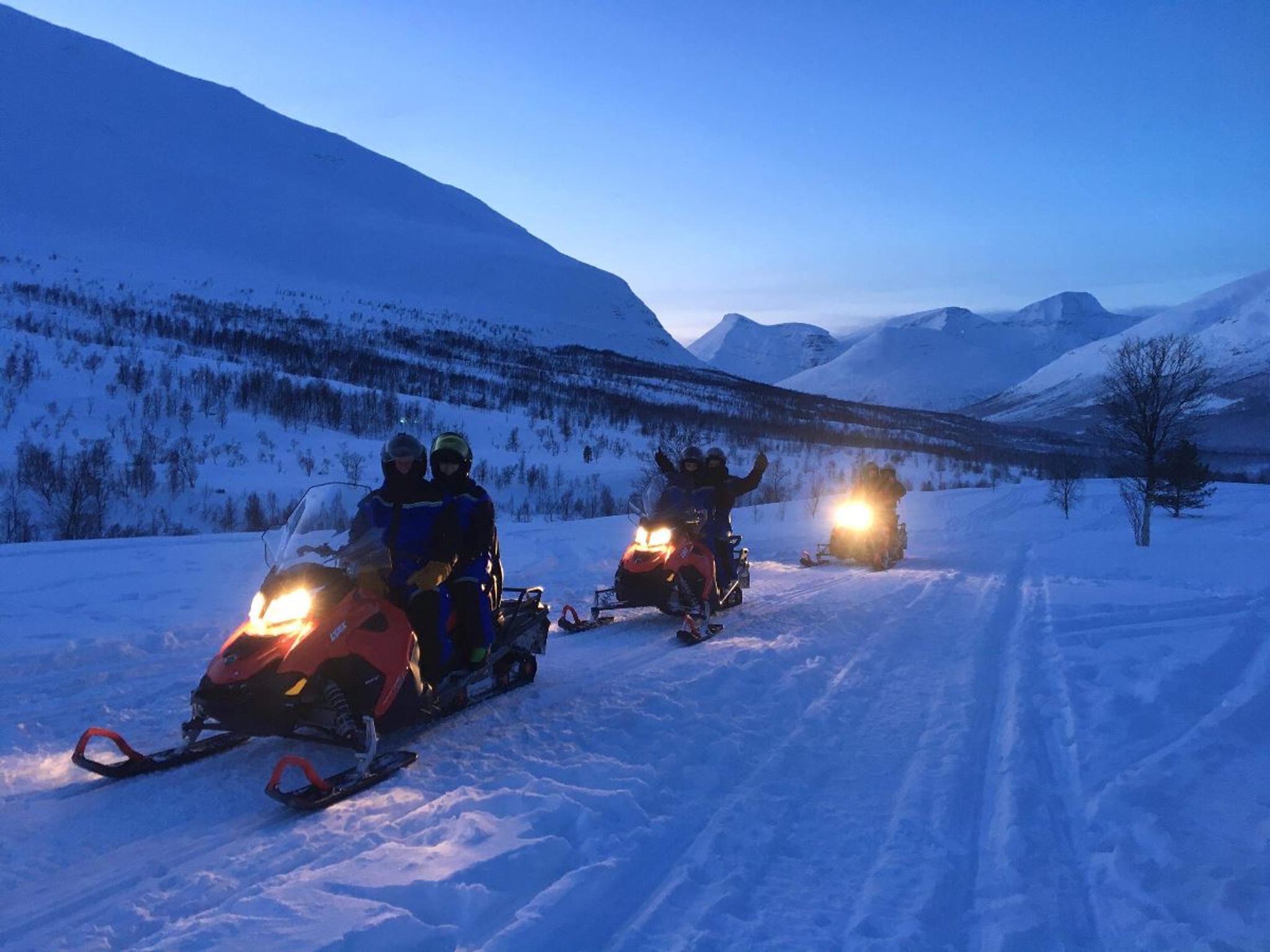 Three snowmobiles driving in the twilight