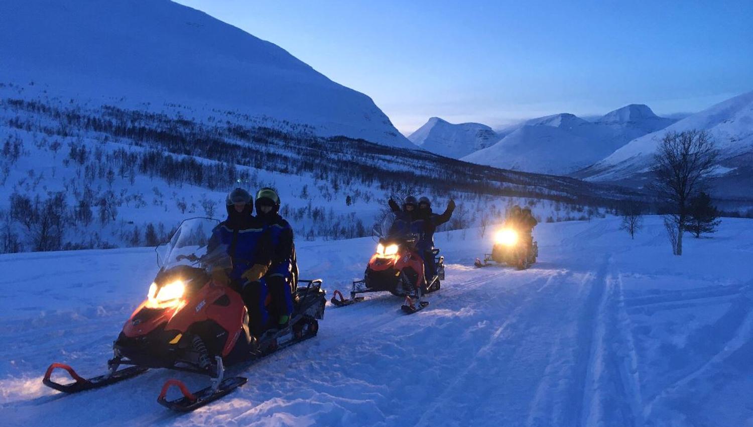 Three snowmobiles driving in the twilight