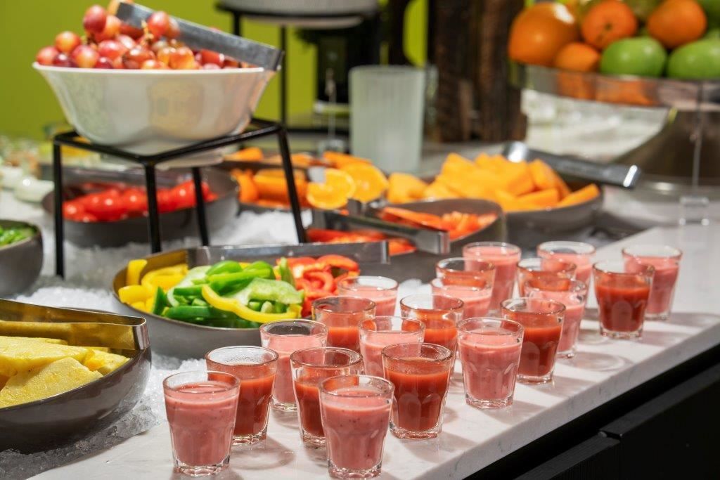 Buffet table with fruit, vegetables, and small glasses of pink smoothie.