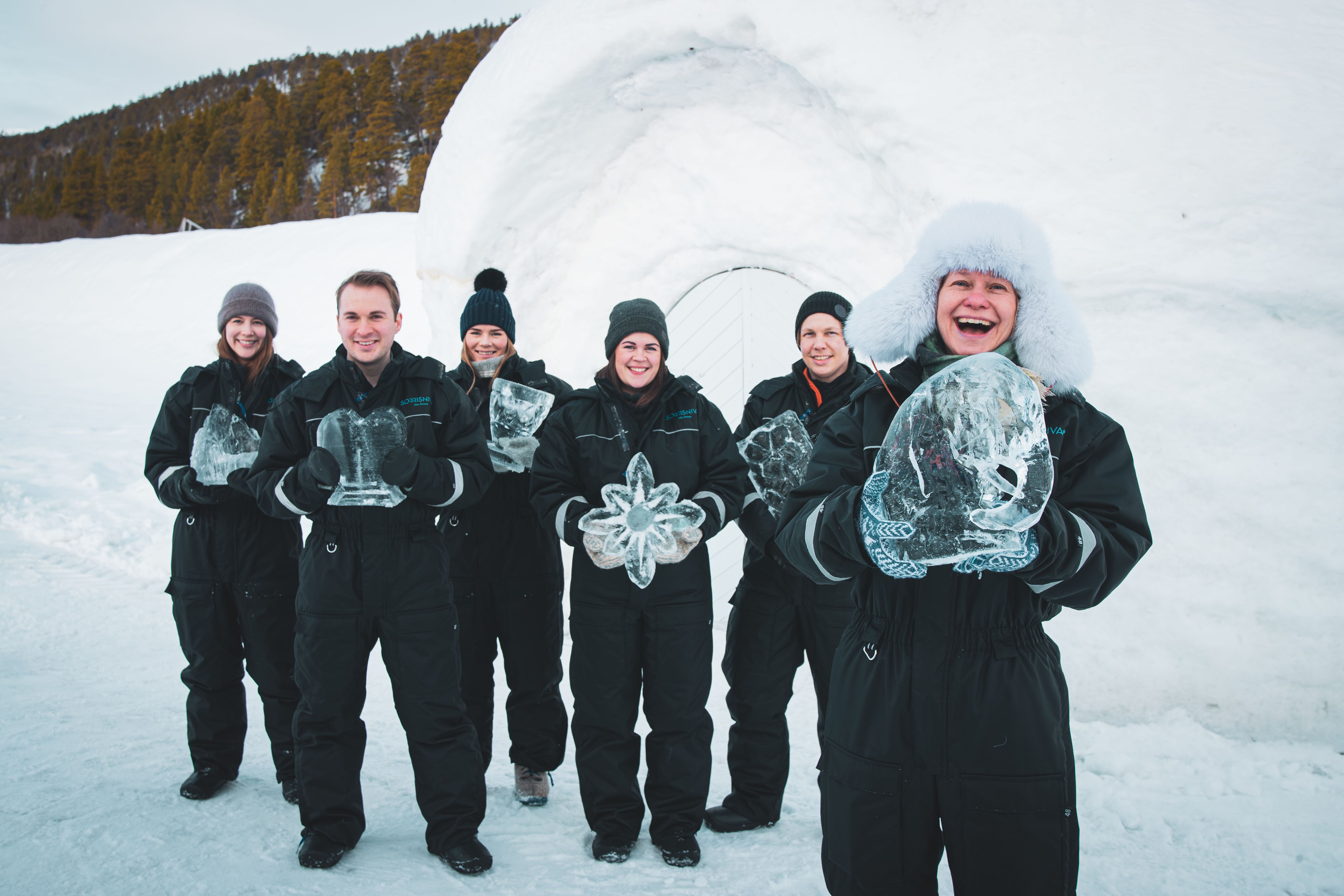 Un groupe de six personnes posant avec des sculptures de glace dans un paysage enneigé.