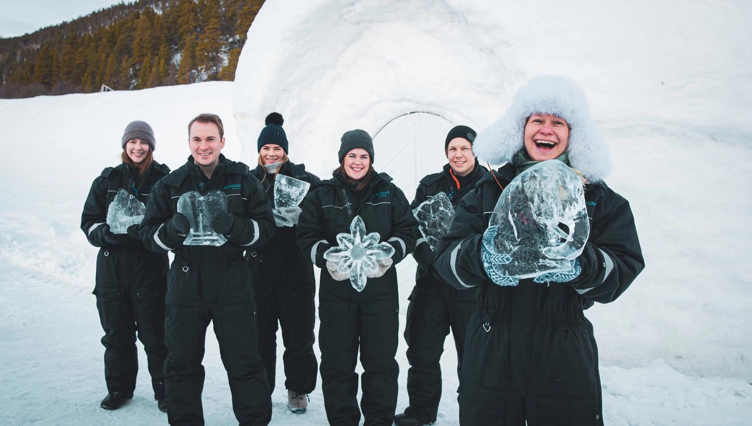 Un groupe de six personnes posant avec des sculptures de glace dans un paysage enneigé.