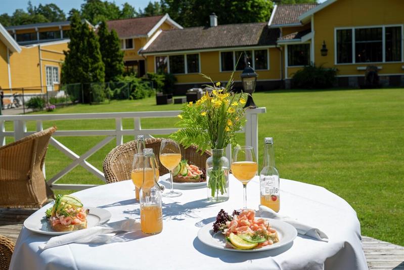 Utendørs servering i hagen på Hankø Hotell & Spa, med dekket bord, mat og drikke foran de gule hotellbygningene.
