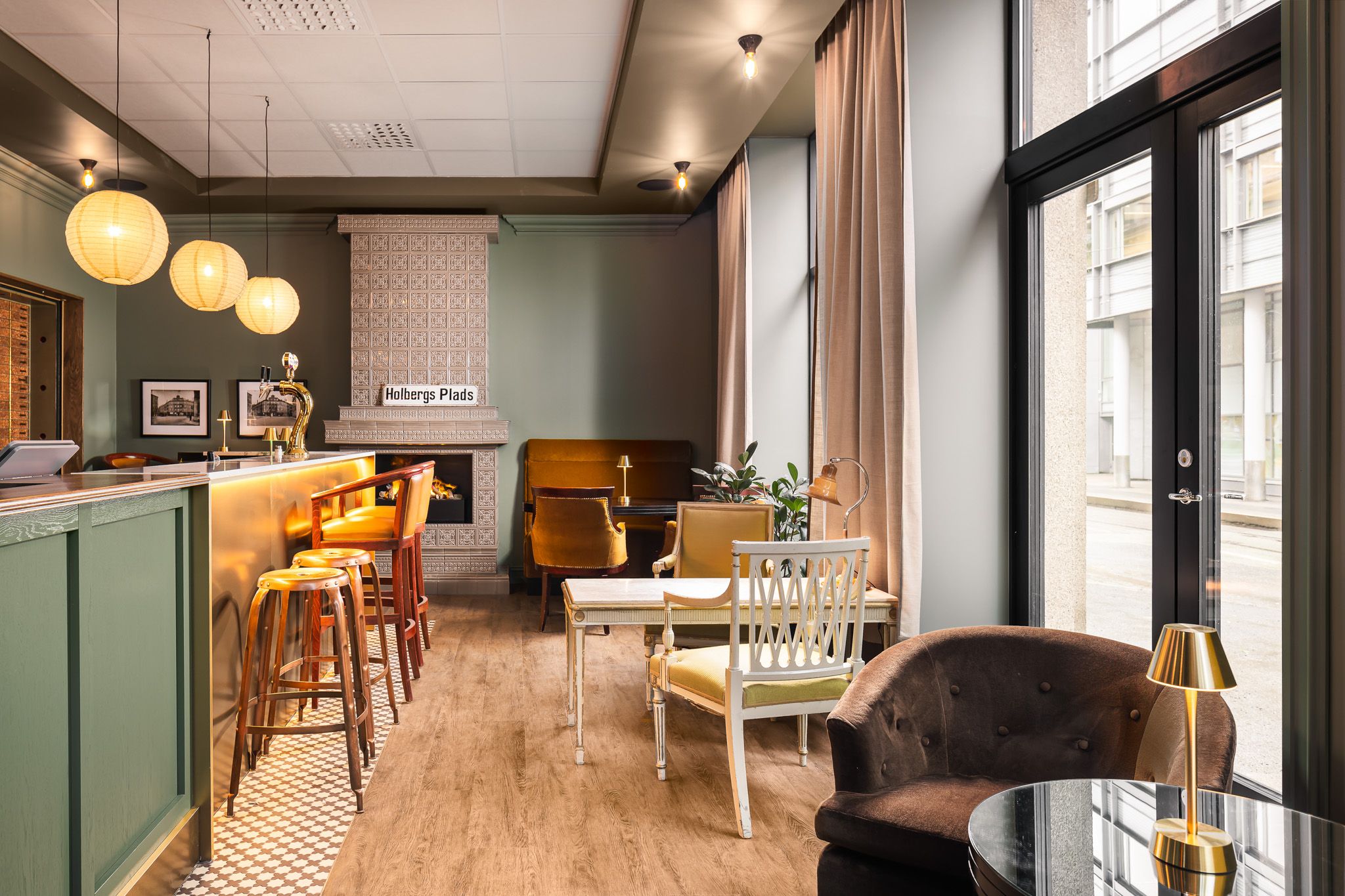A lobby bar with a fireplace, counter, armchairs, tables, and green-painted walls.