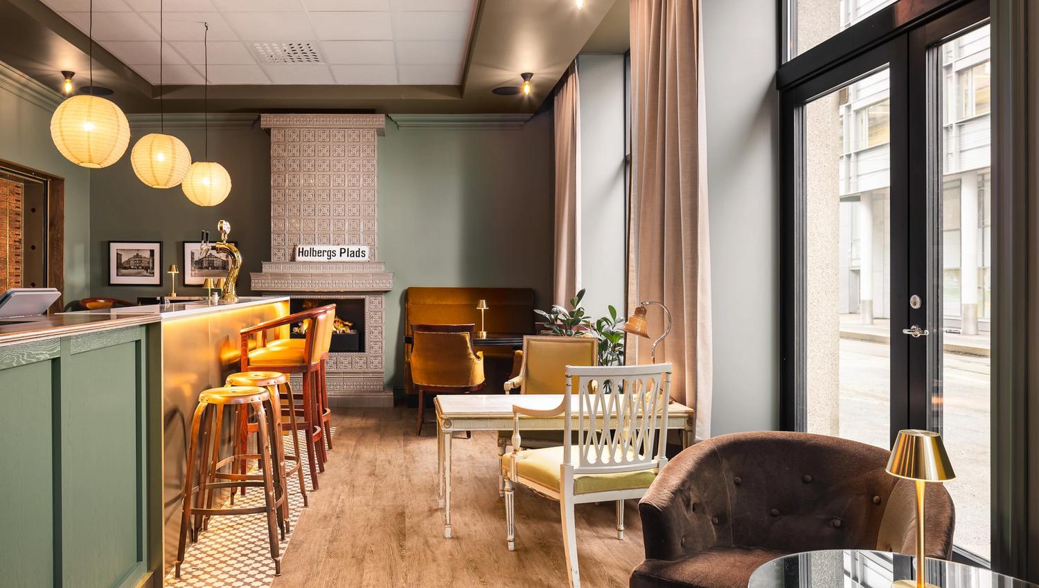 A lobby bar with a fireplace, counter, armchairs, tables, and green-painted walls.