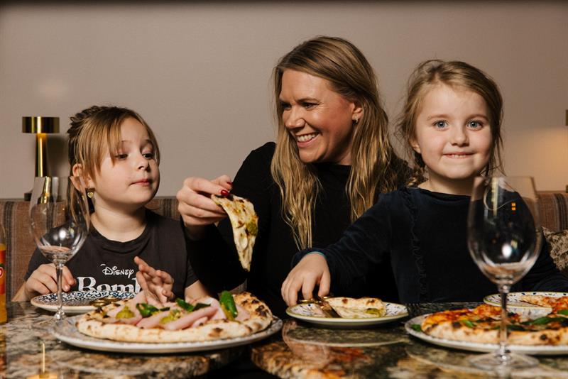 En kvinne og to små jenter som spiser pizza sammen