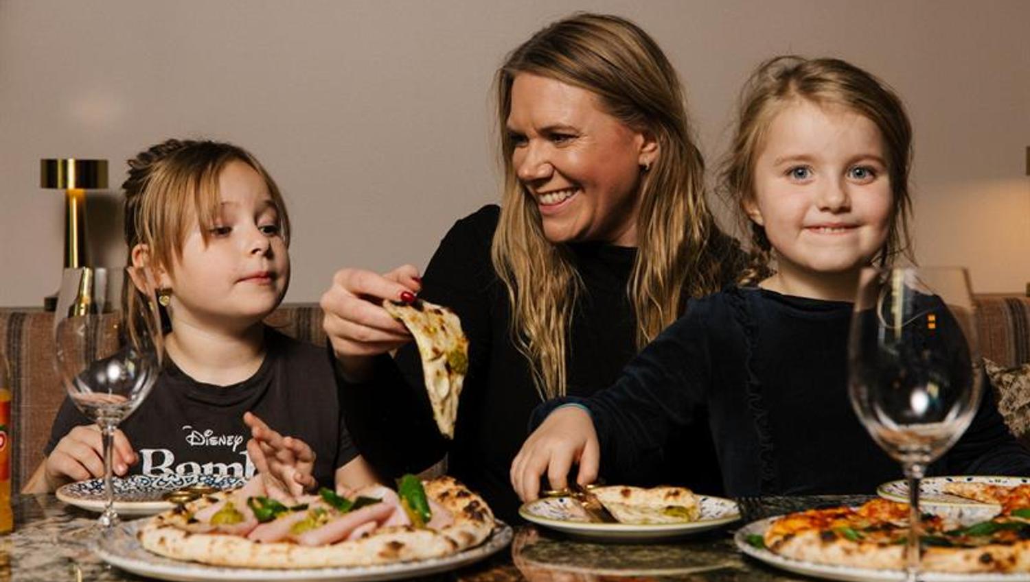 En kvinne og to små jenter som spiser pizza sammen
