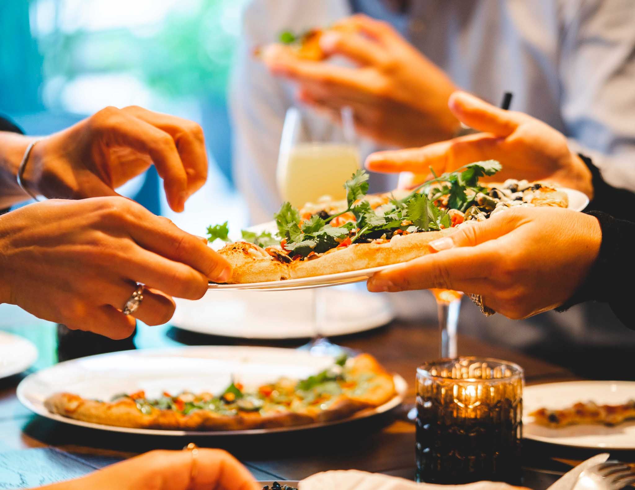 Pizzas on a table and being handed from one set of hands to another