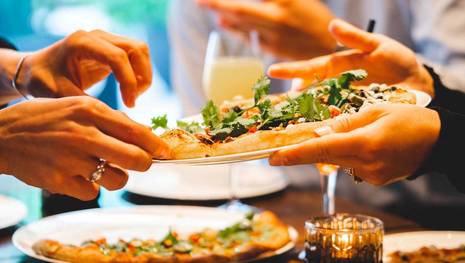 Pizzas on a table and being handed from one set of hands to another