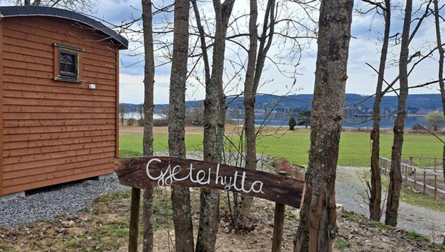 Wooden sign reading Gjeterhytta next to a newly built mini cabin surrounded by trees and open landscape