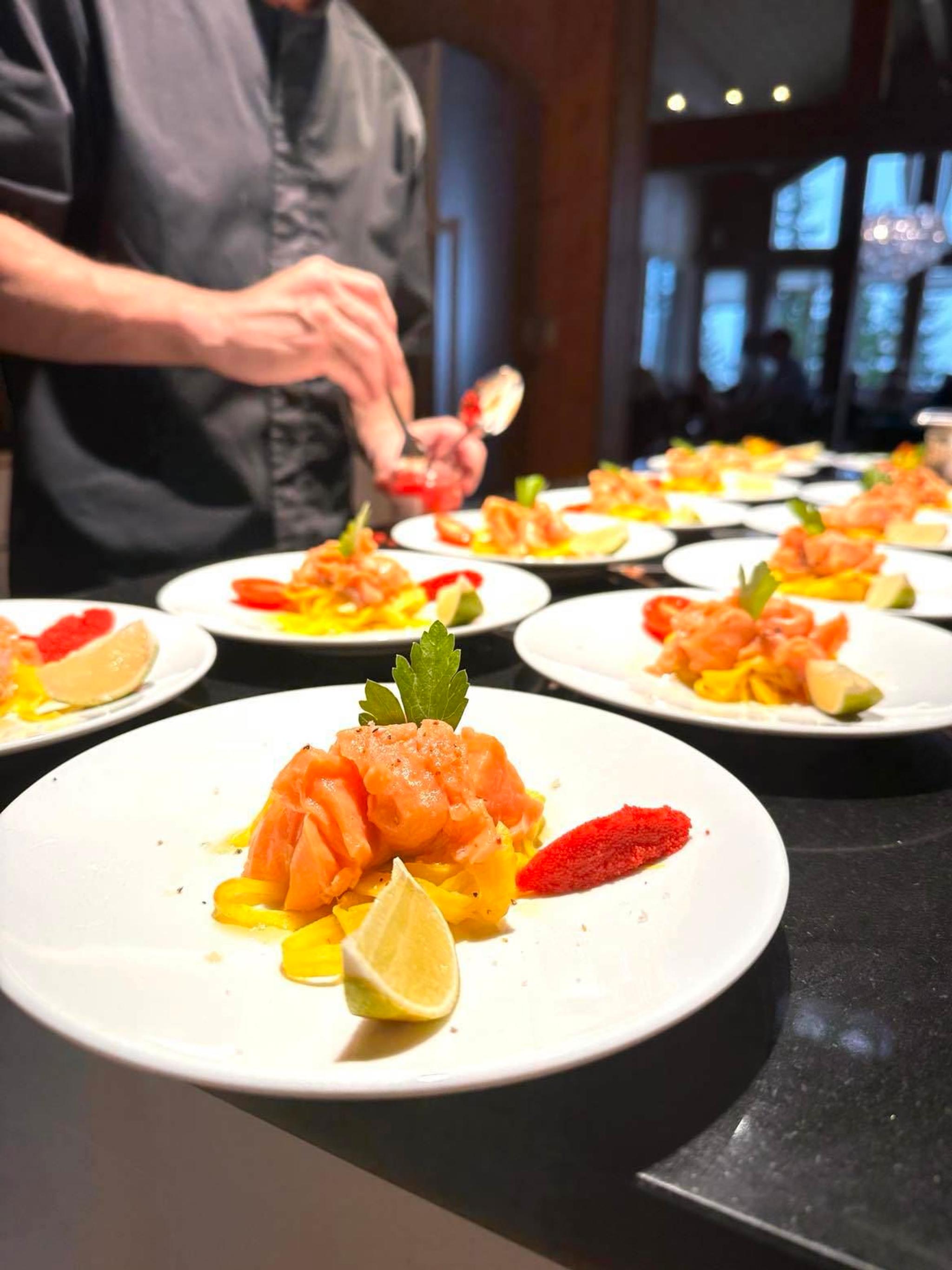 Kokk anretter flere hvite tallerkener med rå laks, sitronbåt, lime, urt og fargerik saus på benk..