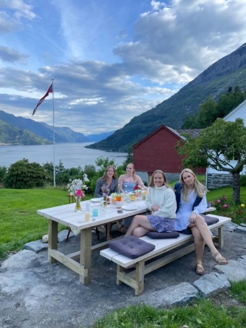 Happy guests enjoying a summer evening at an outdoor picnic table overlooking the fjord at Jaastad Gjestetun.