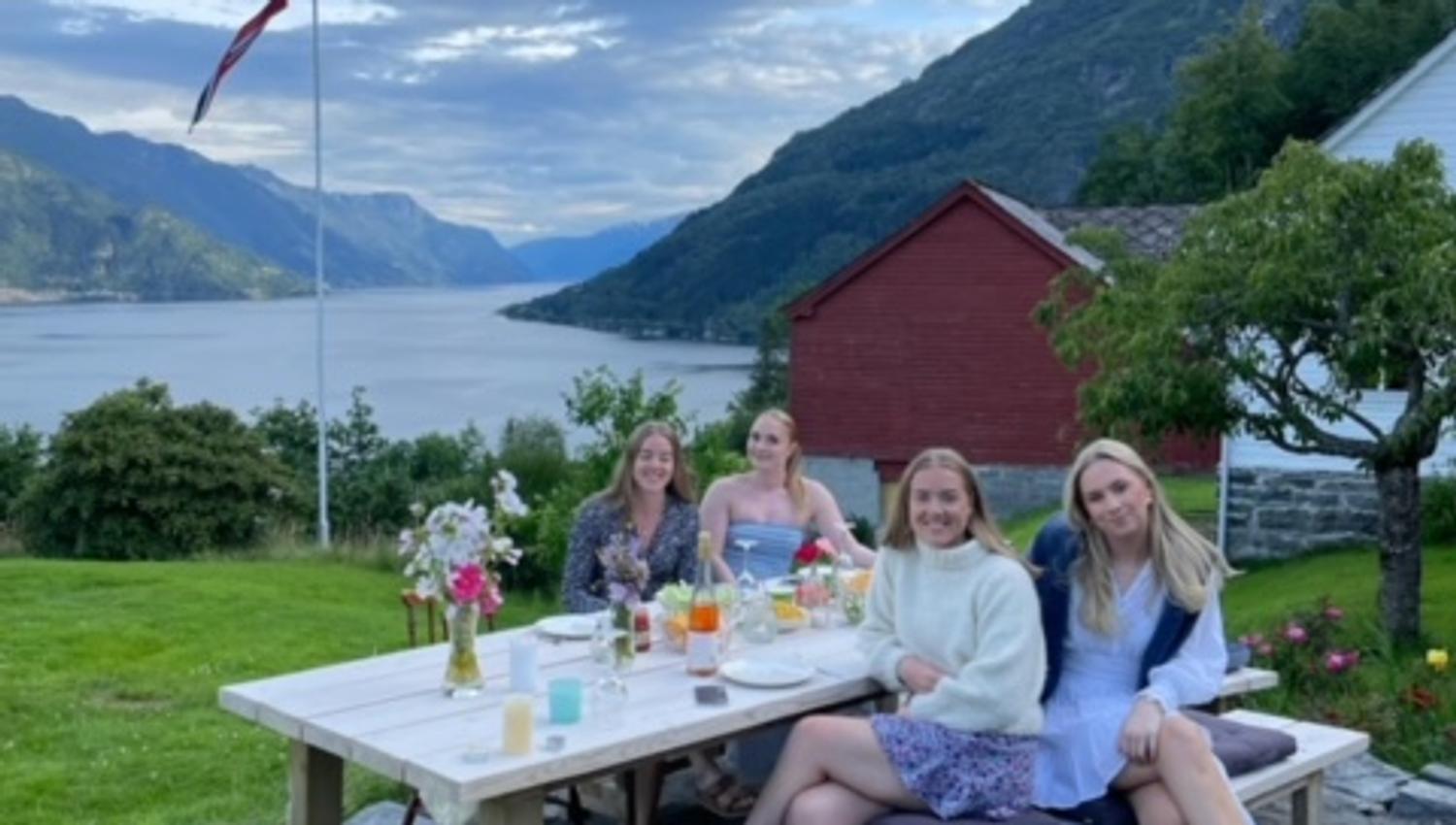 Happy guests enjoying a summer evening at an outdoor picnic table overlooking the fjord at Jaastad Gjestetun.