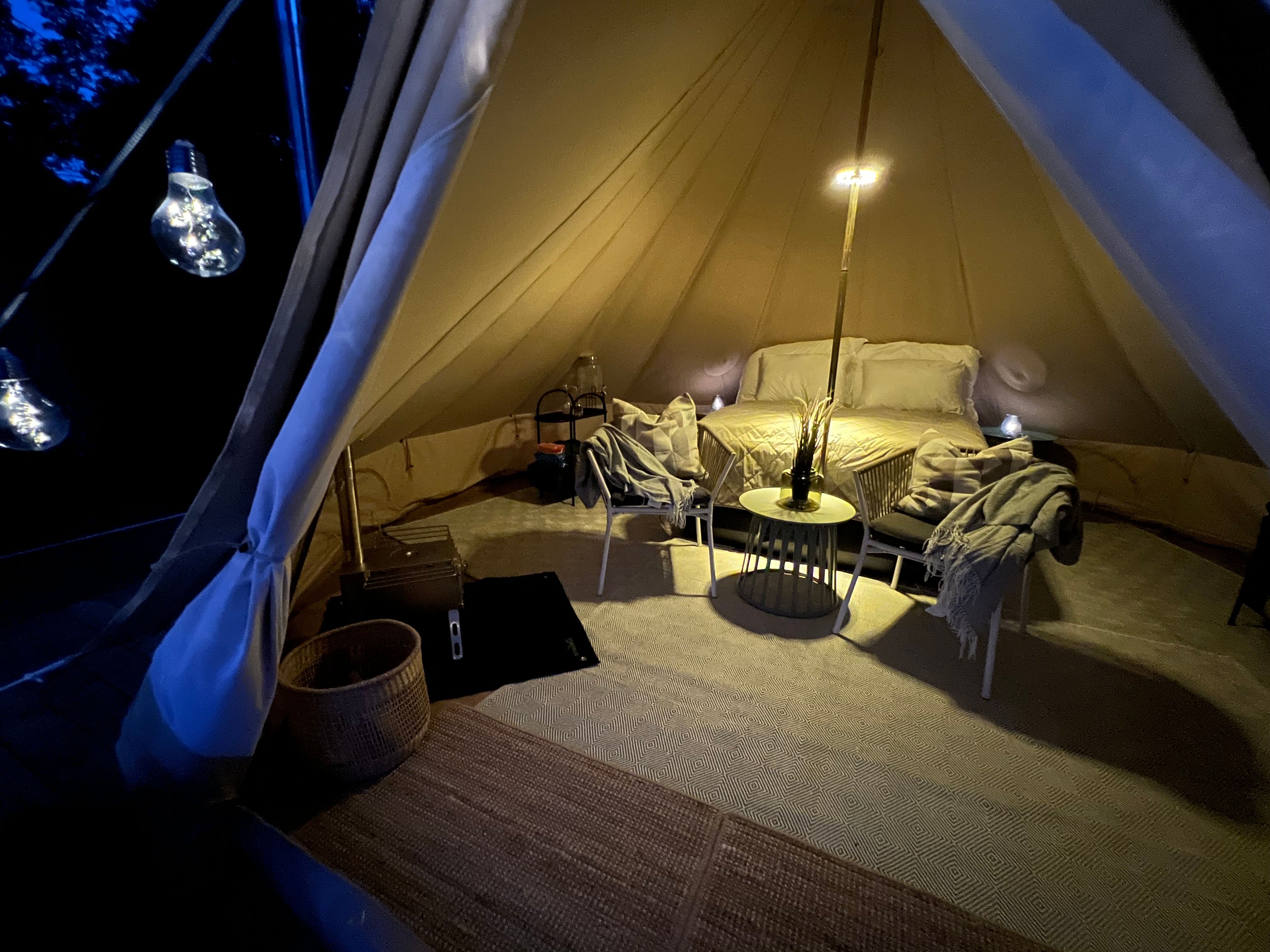 Evening picture from inside the Galmping tent, with a made-up bed, chairs and table