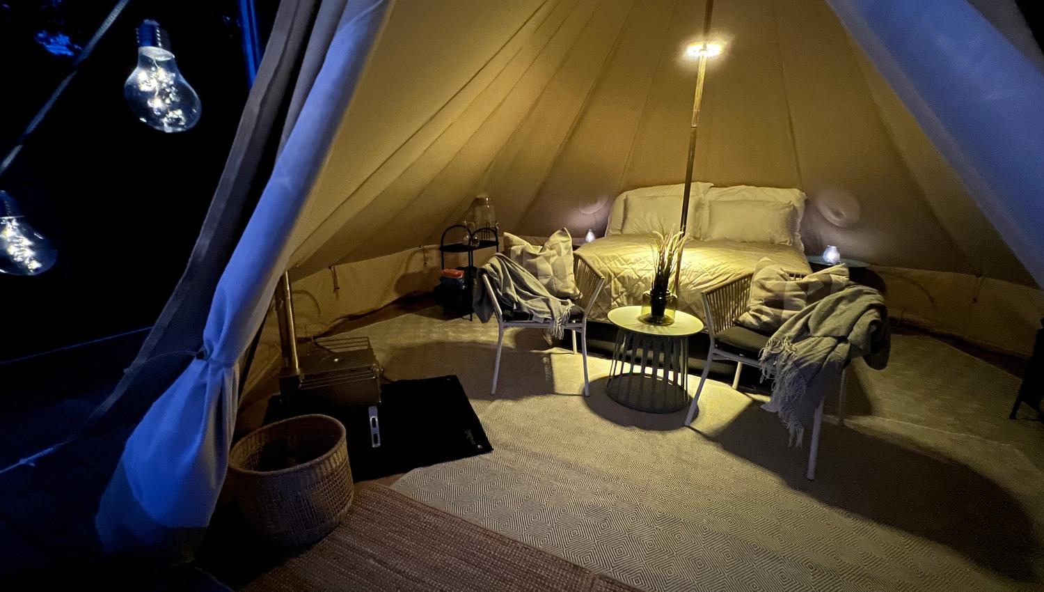 Evening picture from inside the Galmping tent, with a made-up bed, chairs and table