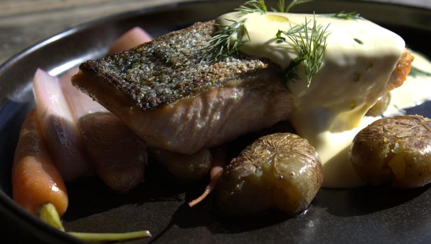Pan-fried fish served with new potatoes, vegetables and sauce. Plated for table service.