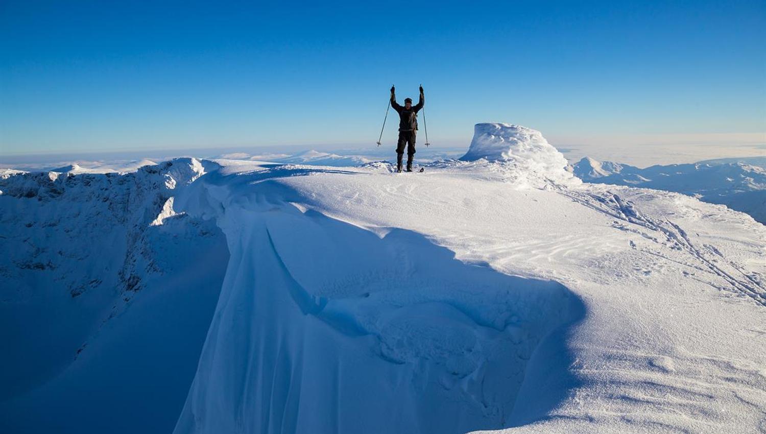 Bergskiläufer auf einem Gipfel mit Schneeüberhang und Abgrund