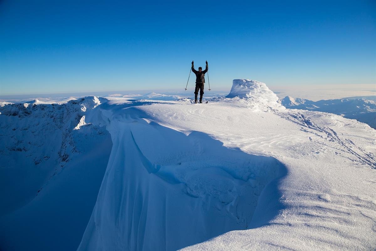 Bergskiläufer auf einem Gipfel mit Schneeüberhang und Abgrund