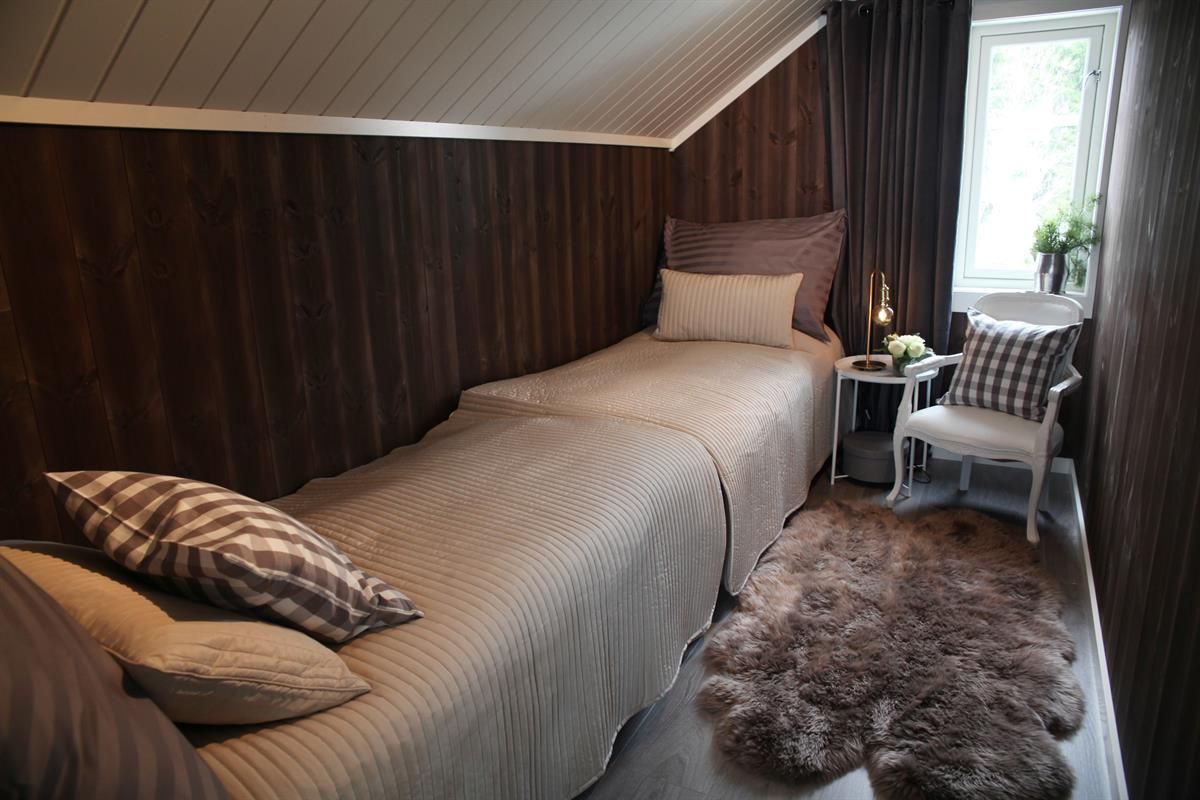 A narrow bedroom with a single bed, pillows, and a small table by the window.