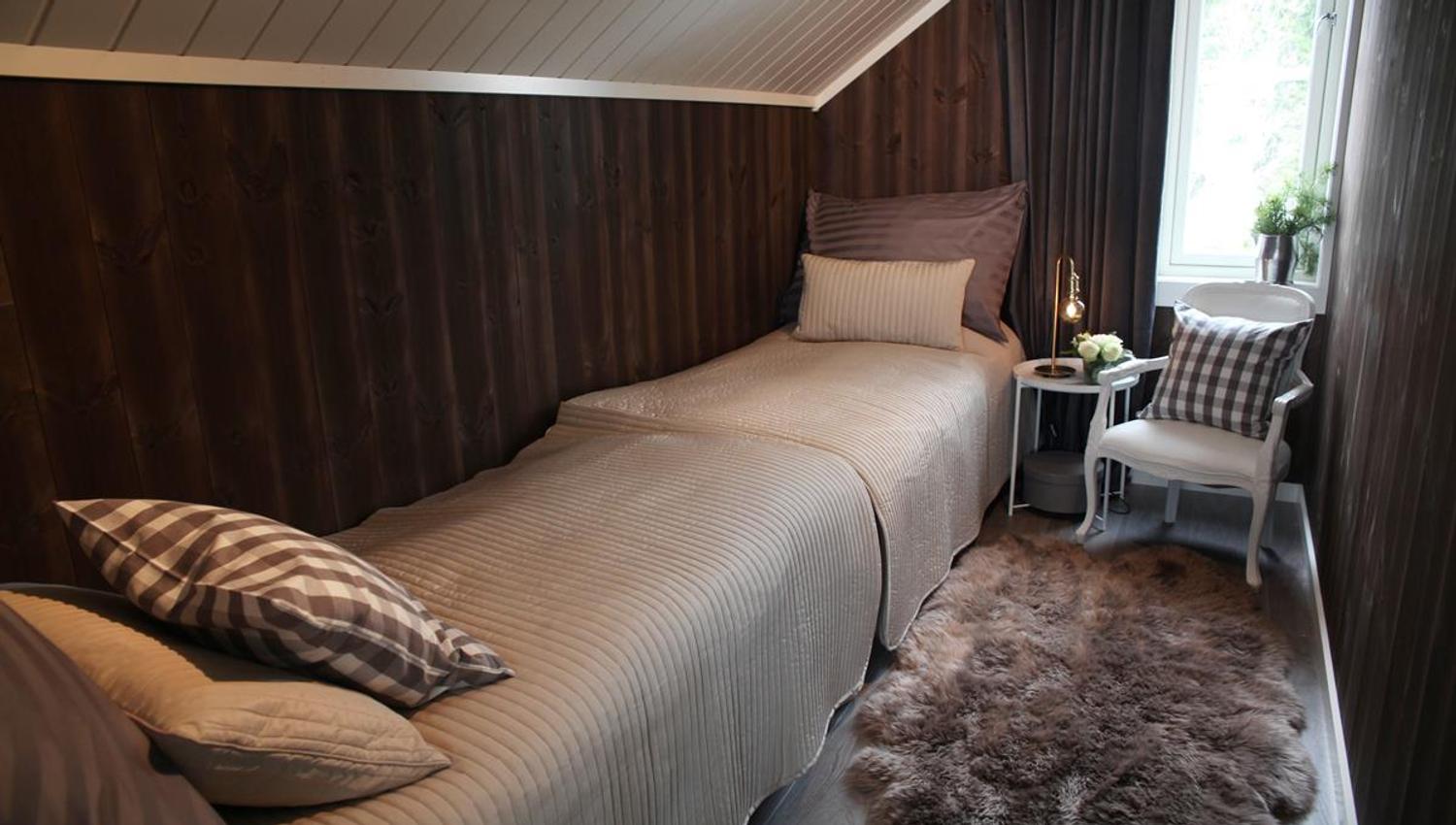 A narrow bedroom with a single bed, pillows, and a small table by the window.