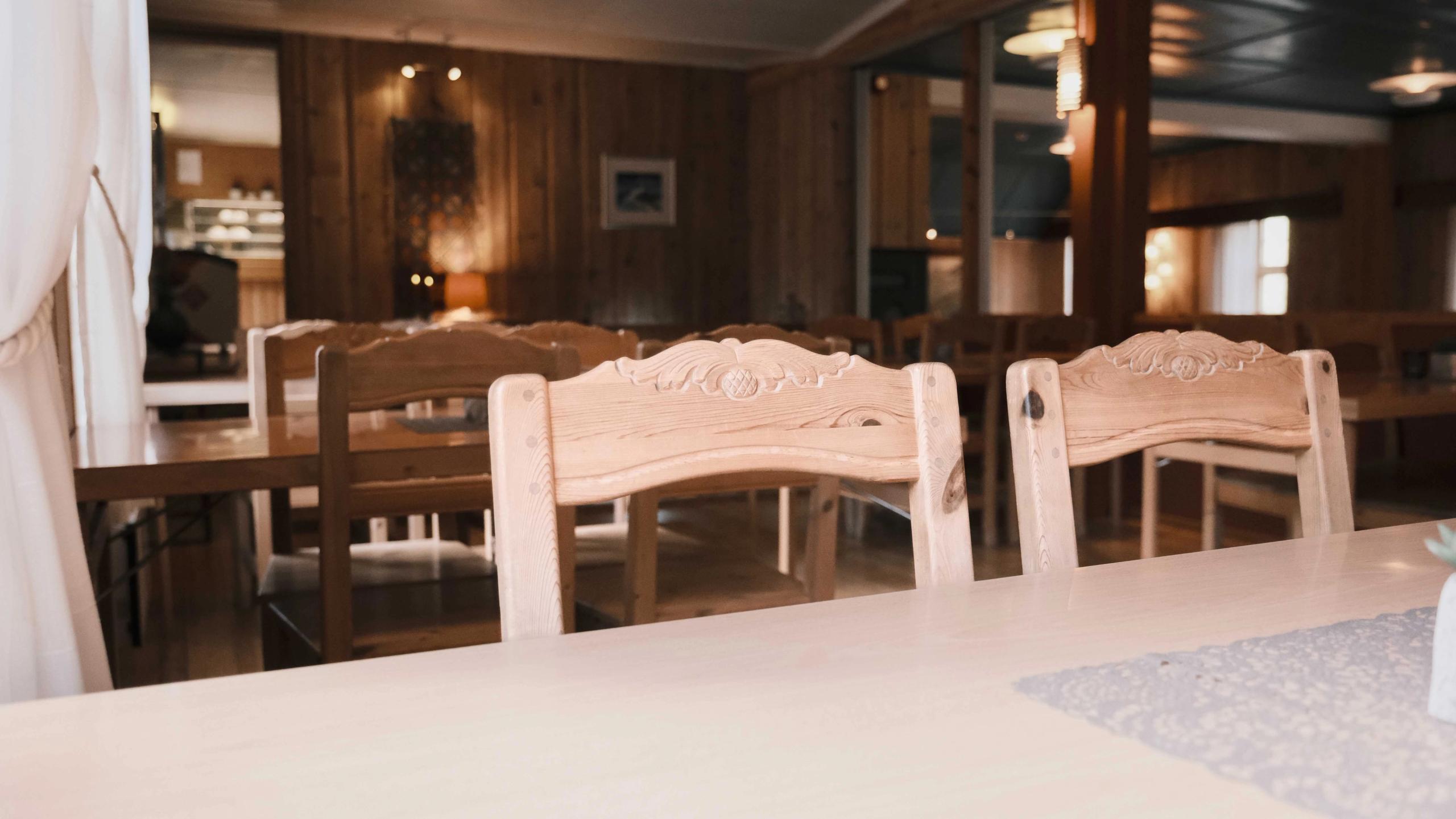 Empty rustic dining room with wooden chairs and tables, warm lamps, and wood-paneled walls with soft daylight..