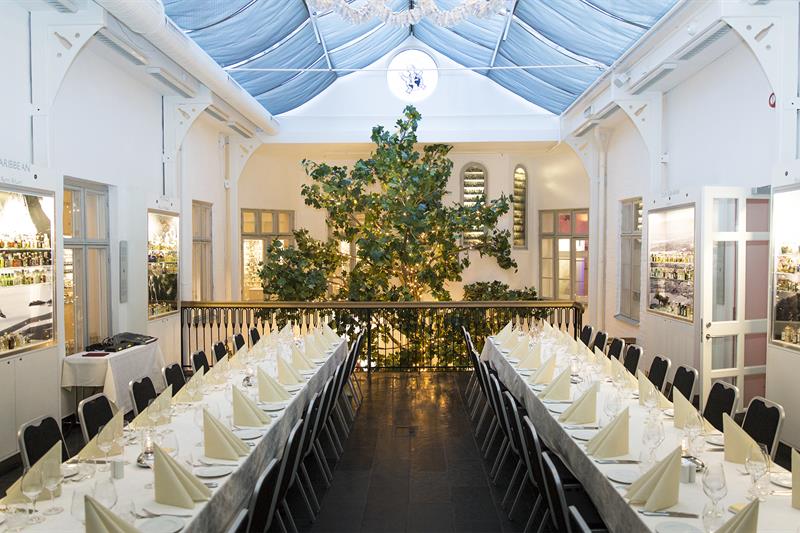 The banqueting hall with two long tables with white tablecloths and a large tree in the background