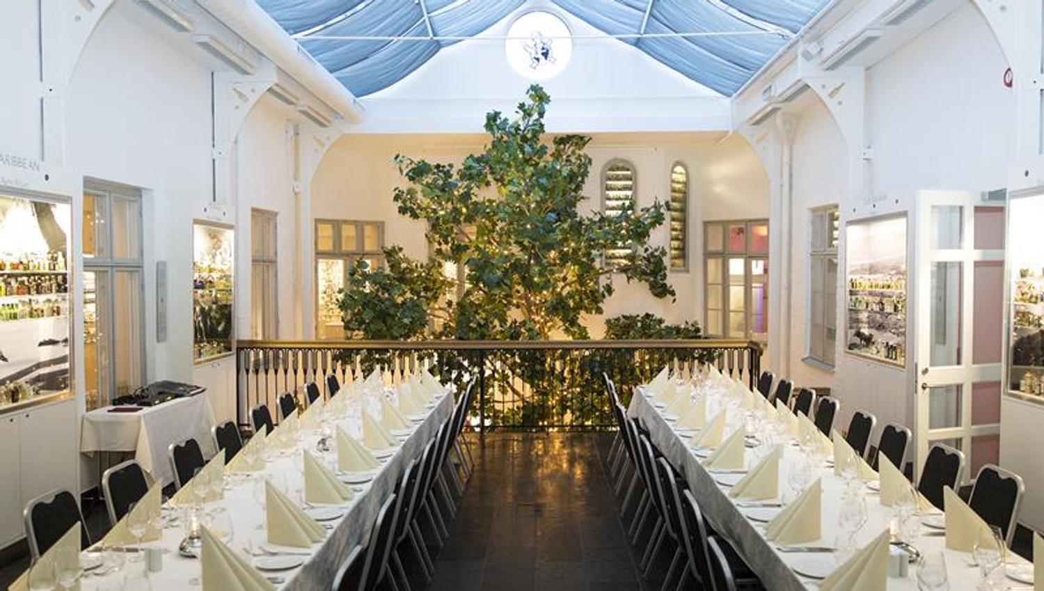 The banqueting hall with two long tables with white tablecloths and a large tree in the background