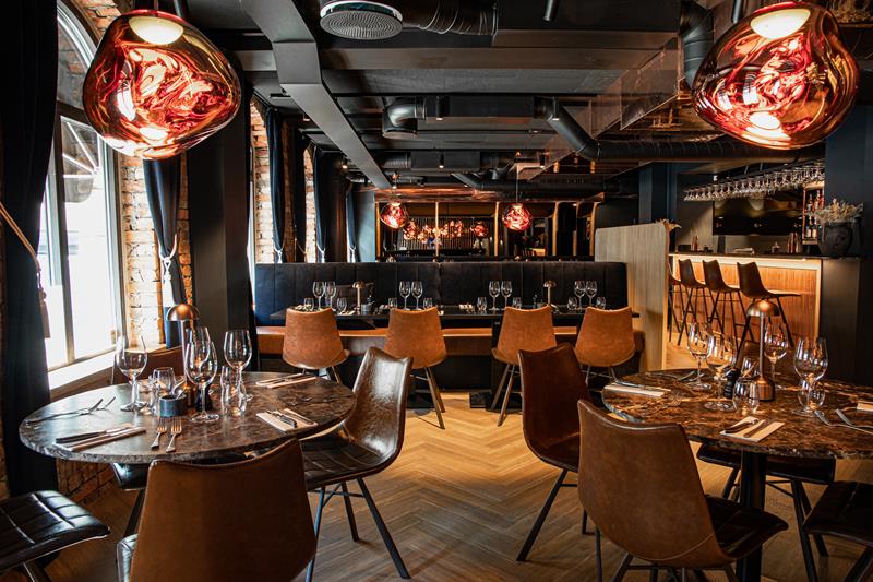 Restaurant interior with round, brown tables, brown chairs and seating section against the wall.