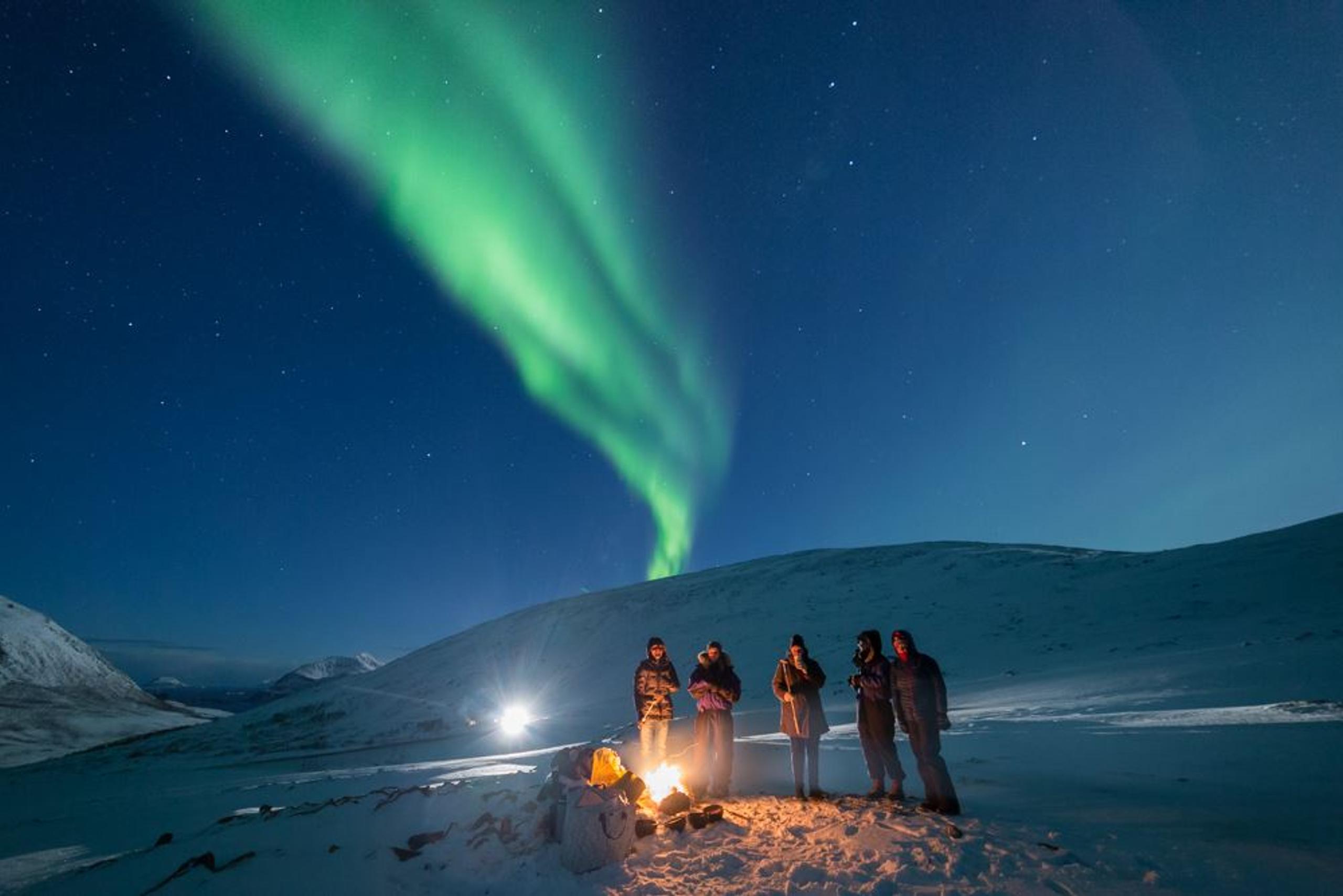 Guests surround the campfire while the Northern Lights fly by overhead