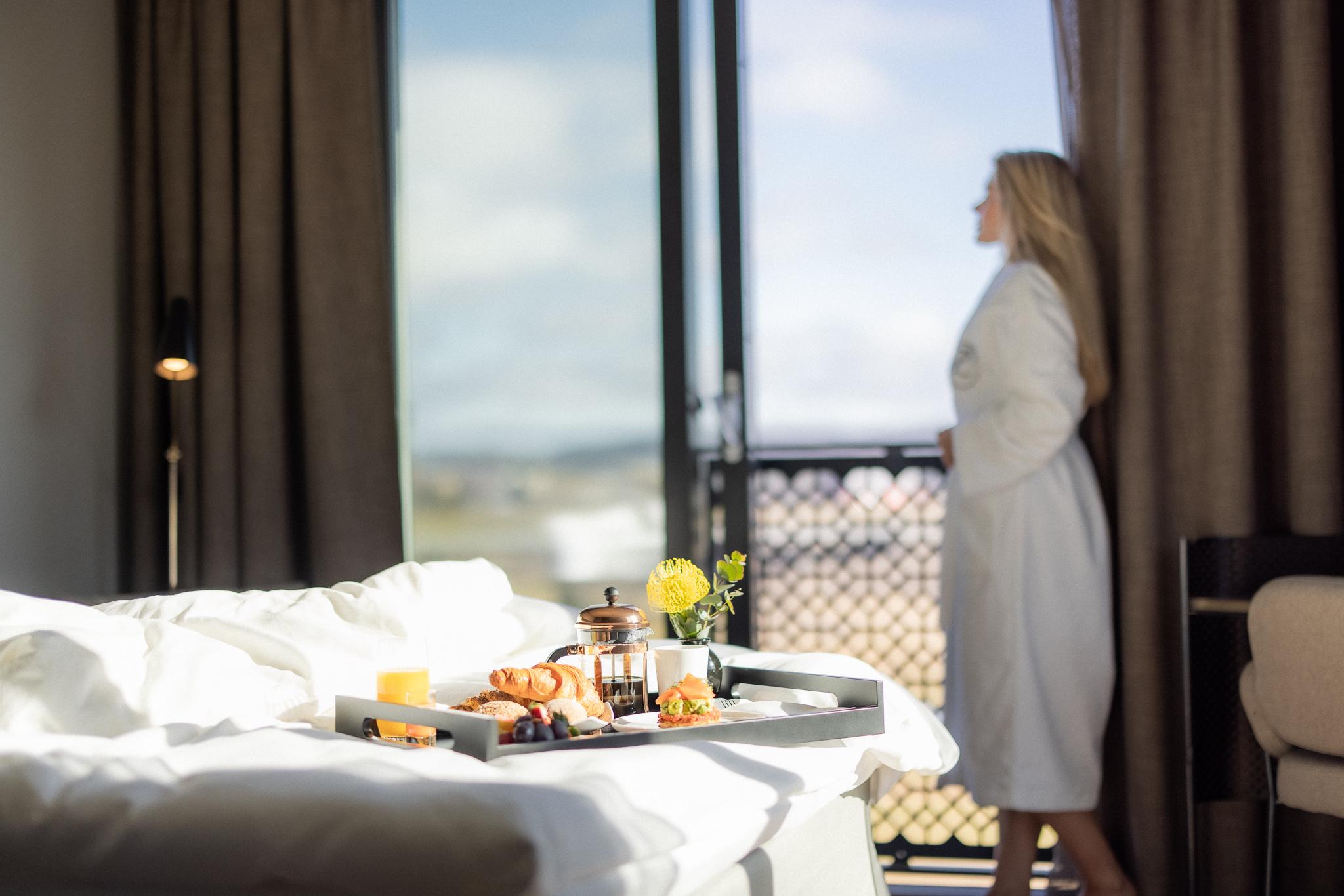 Lady looking out of å window breakfast tray on the bed 