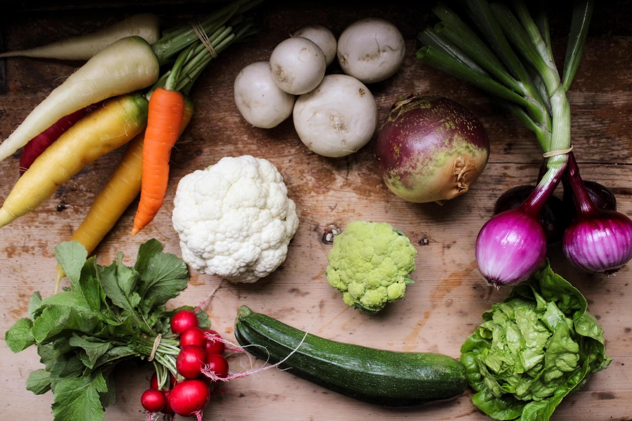 Top-down view of assorted fresh vegetables on a rustic wooden surface, including carrots, onions, radishes, and cauliflower..