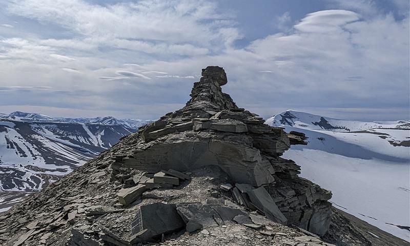 A mountain ridge with the rock formation known as Trolllsteinen, with lightly snow-covered mountains and a cloudy sky in the background