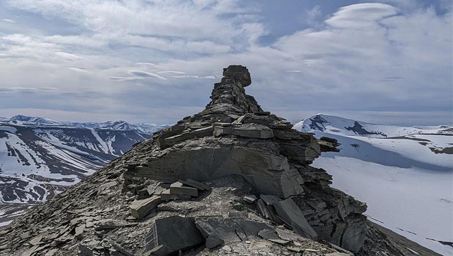 A mountain ridge with the rock formation known as Trolllsteinen, with lightly snow-covered mountains and a cloudy sky in the background
