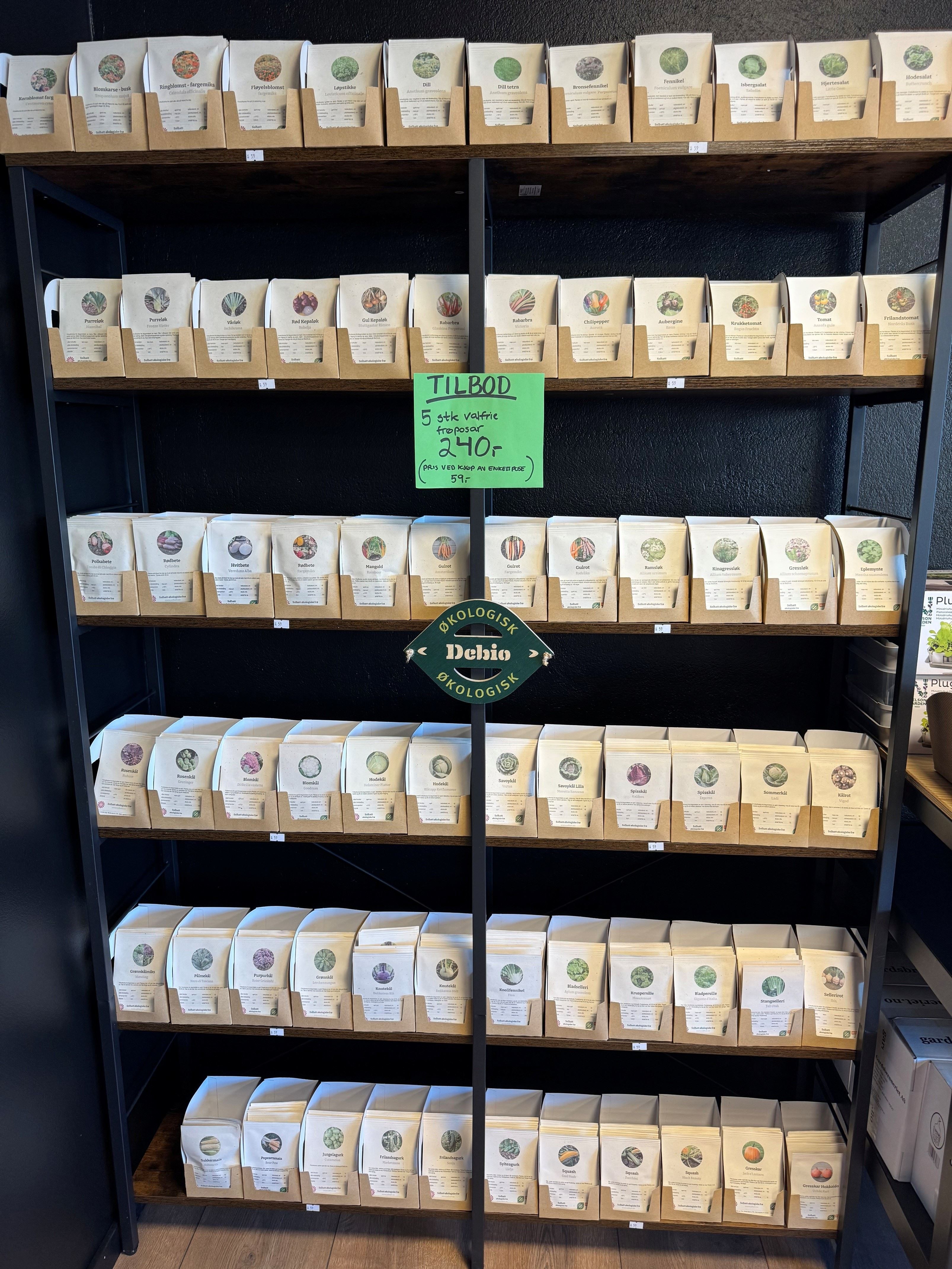 Metal shelving unit filled with paper seed packets in cardboard holders, with a green sale sign on front.