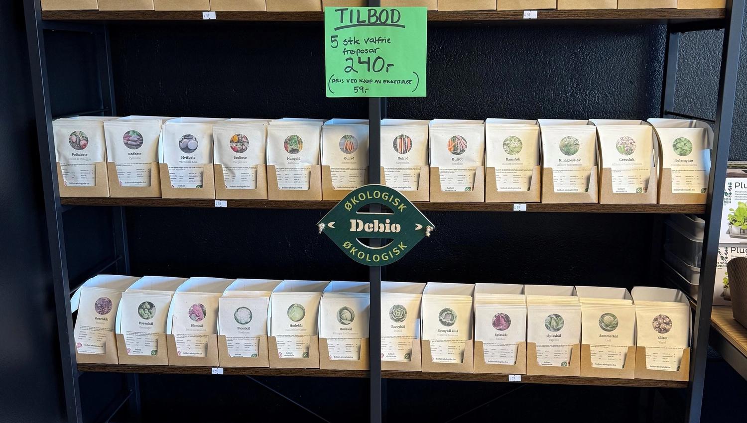 Metal shelving unit filled with paper seed packets in cardboard holders, with a green sale sign on front.