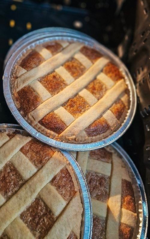 Close-up of three baked lattice-crust pies in round foil pans stacked together, with browned crusts and dark filling.
