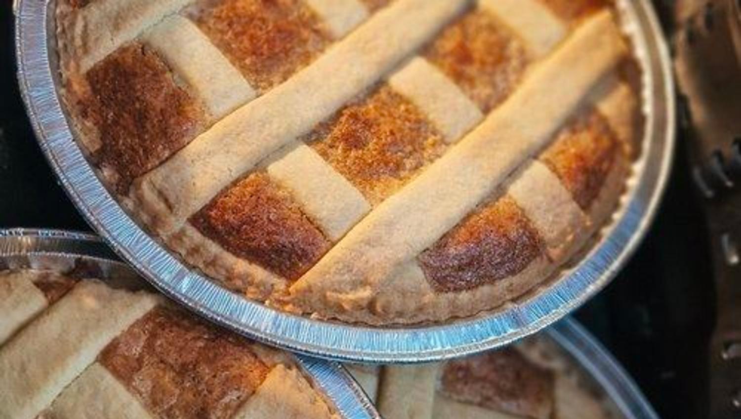 Close-up of three baked lattice-crust pies in round foil pans stacked together, with browned crusts and dark filling.