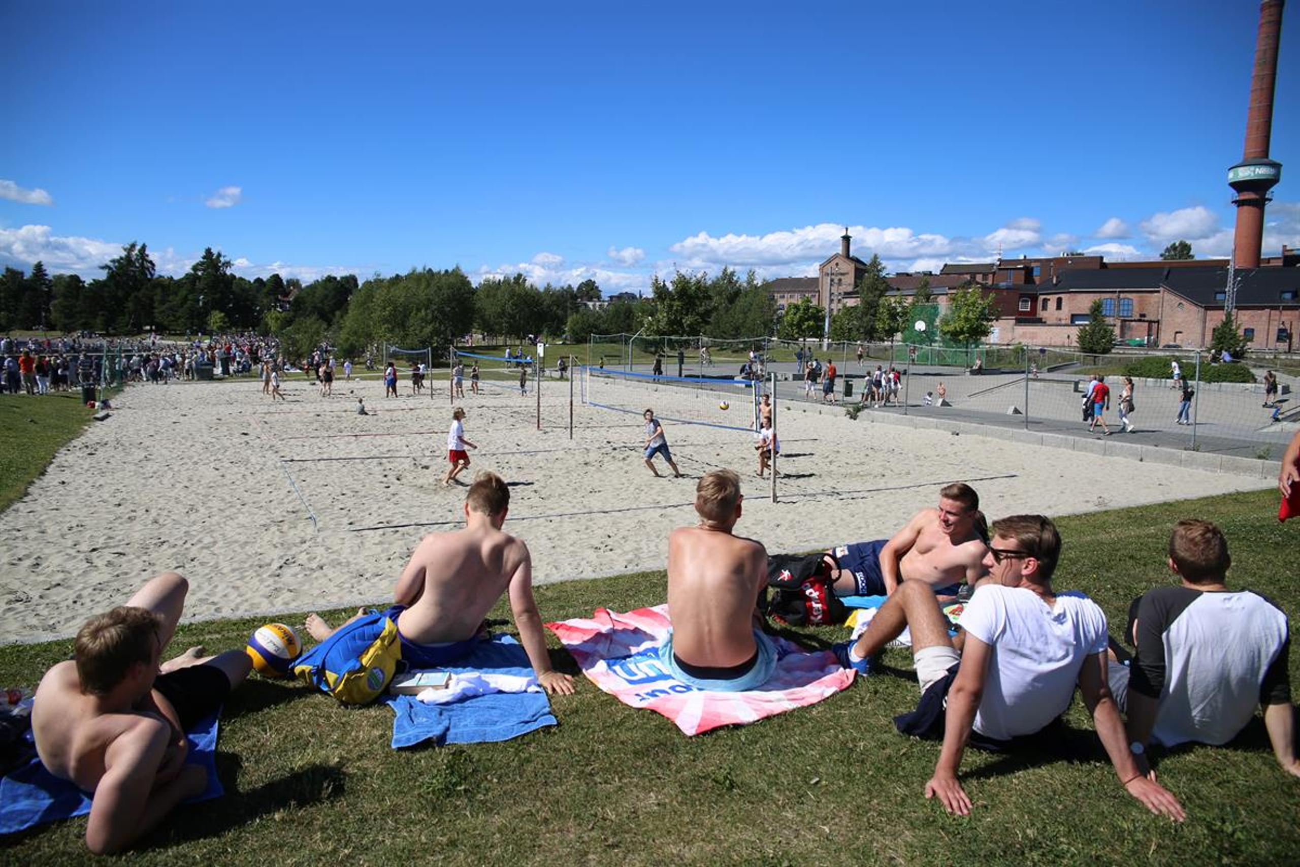 Sandvolley-bane og ungdom som sitter på gresset på siden