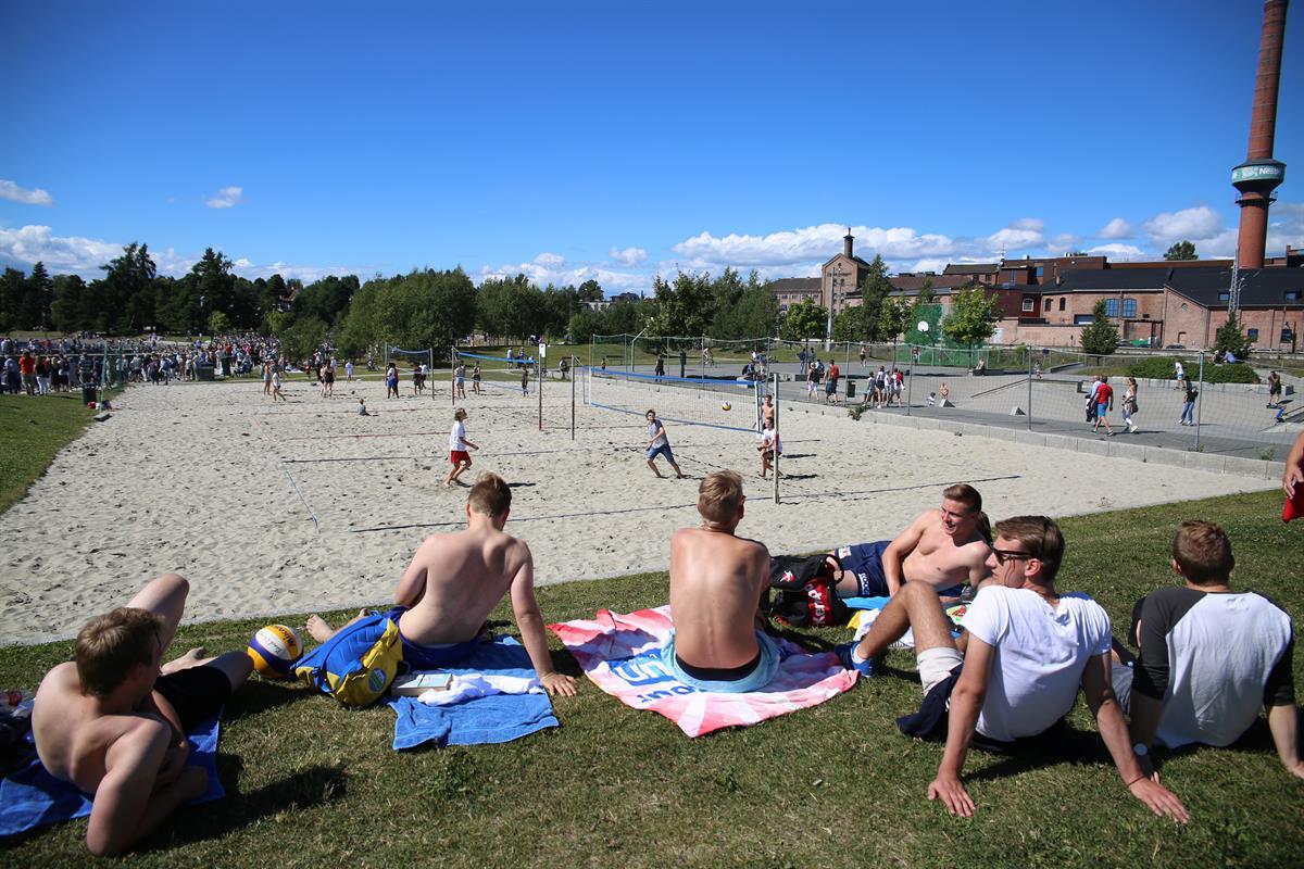 Sandvolley-bane og ungdom som sitter på gresset på siden