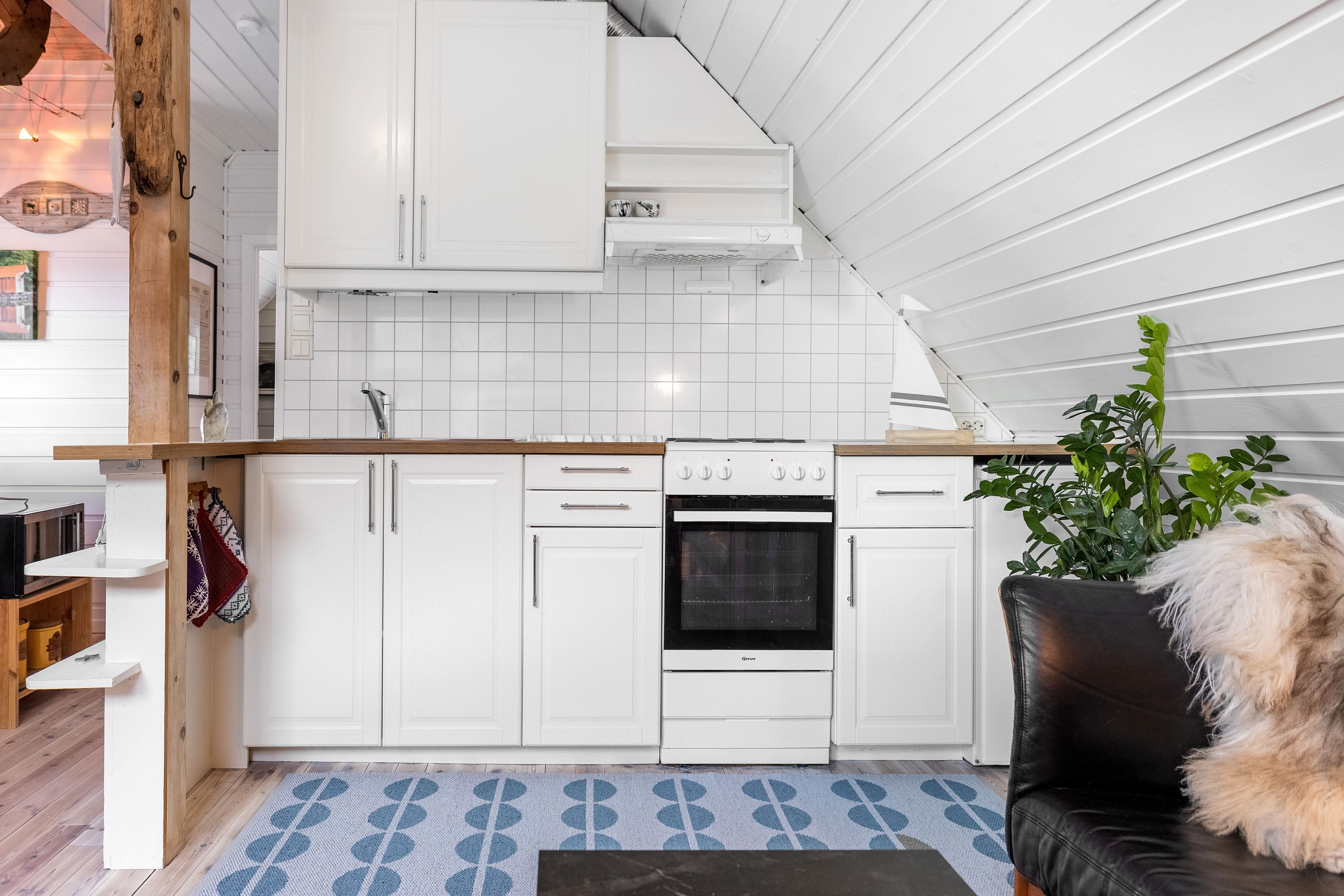 Compact white kitchen with wood countertop, tiled backsplash, stove and sink under a slanted ceiling, plus a plant at the Seahouse at Hornelen Panorama in Bremanger..