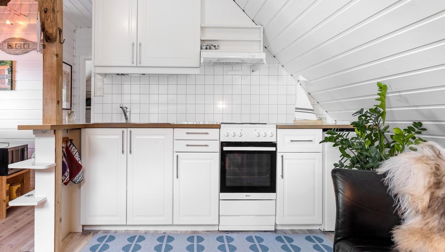 Compact white kitchen with wood countertop, tiled backsplash, stove and sink under a slanted ceiling, plus a plant at the Seahouse at Hornelen Panorama in Bremanger..