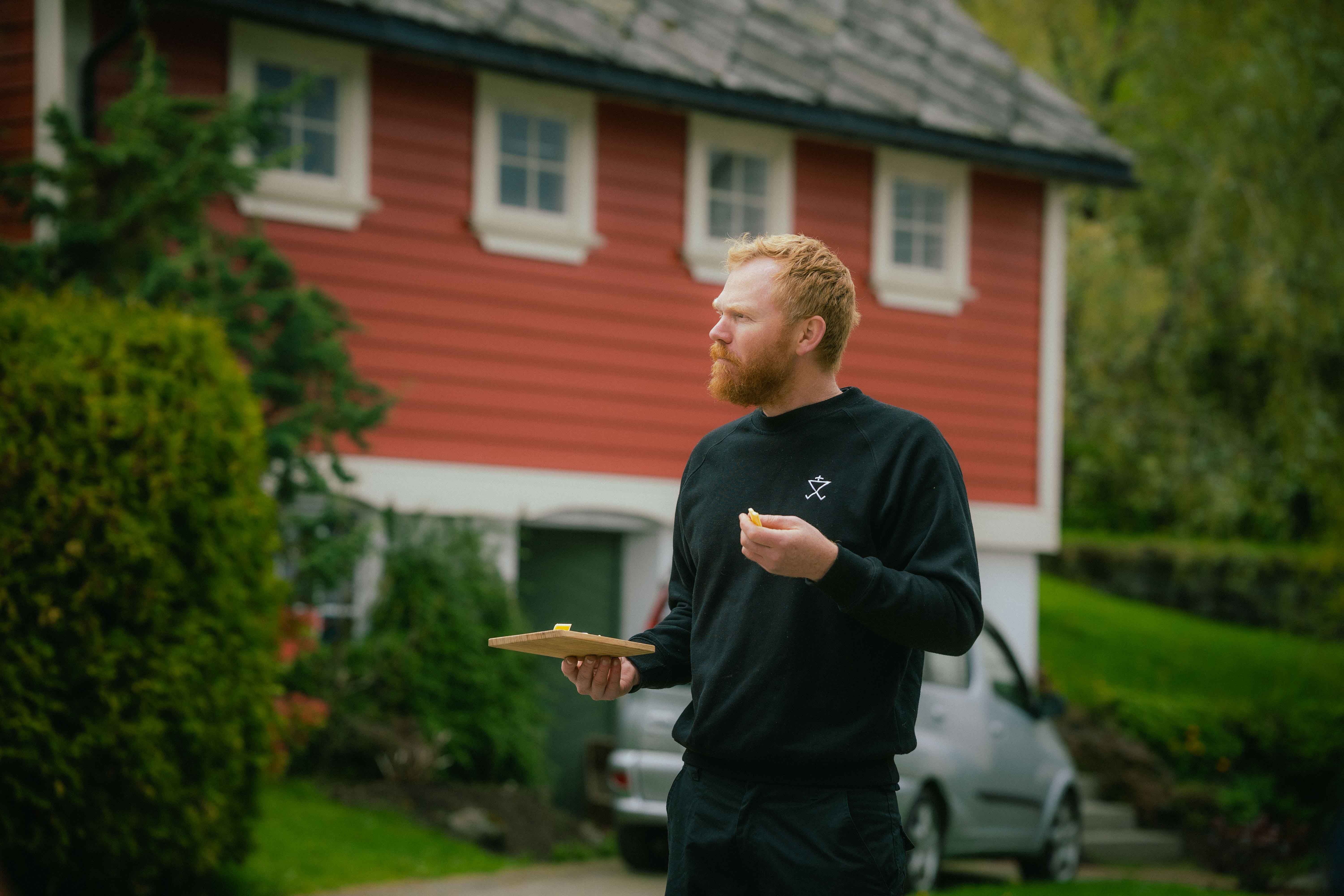 Olav Bleie from Alde tasting cheese in front of a traditional building in Hardanger.