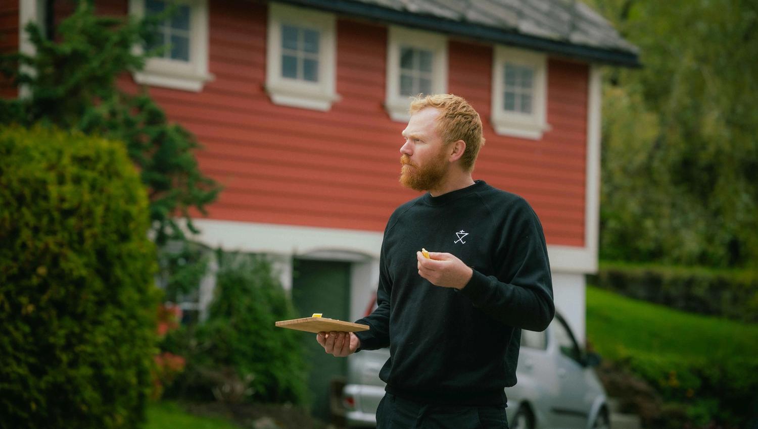 Olav Bleie from Alde tasting cheese in front of a traditional building in Hardanger.