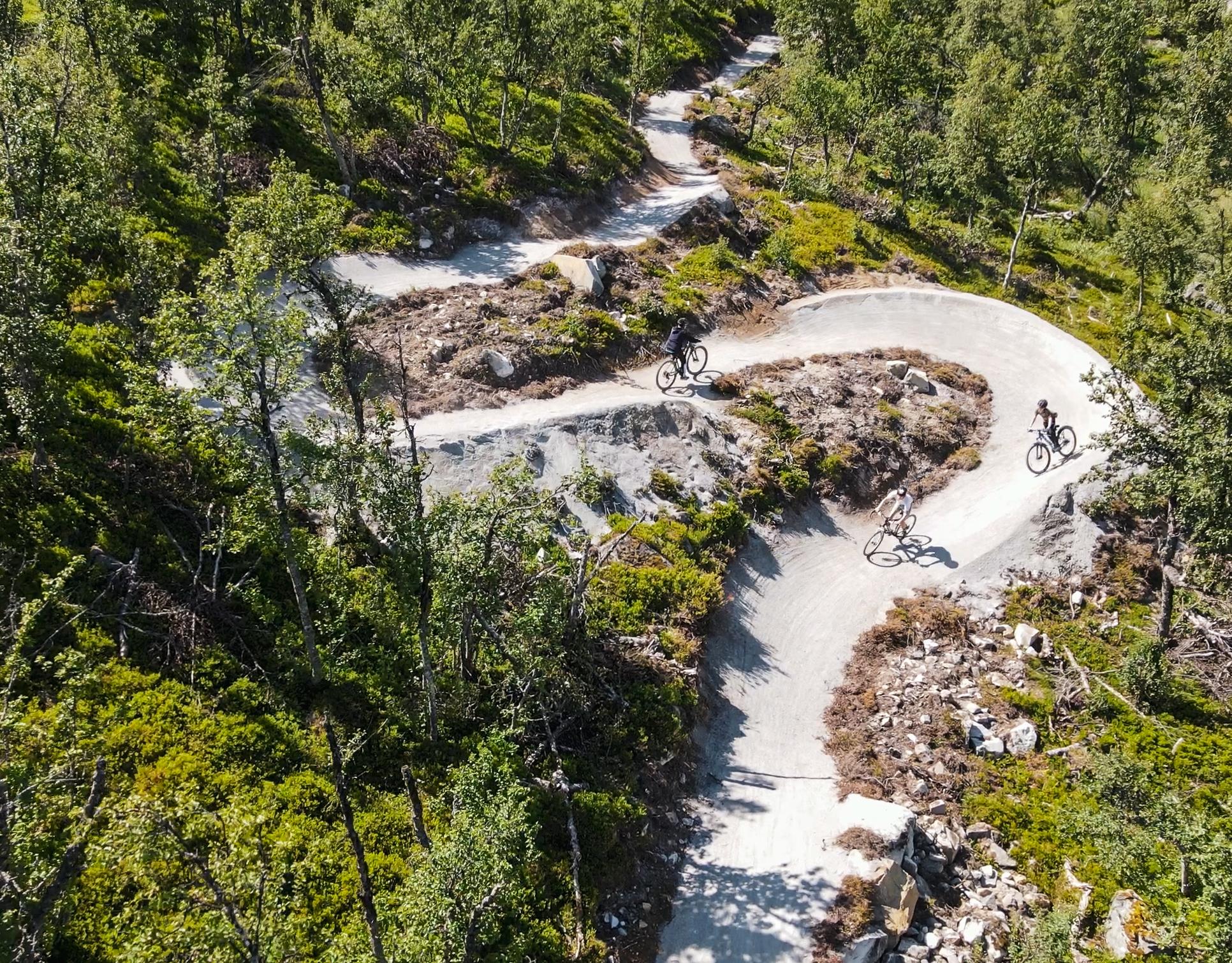 Drone picture from the summer with the lift-based cycle path Flow Motion. There are three cyclists heading down a winding path through the green fores