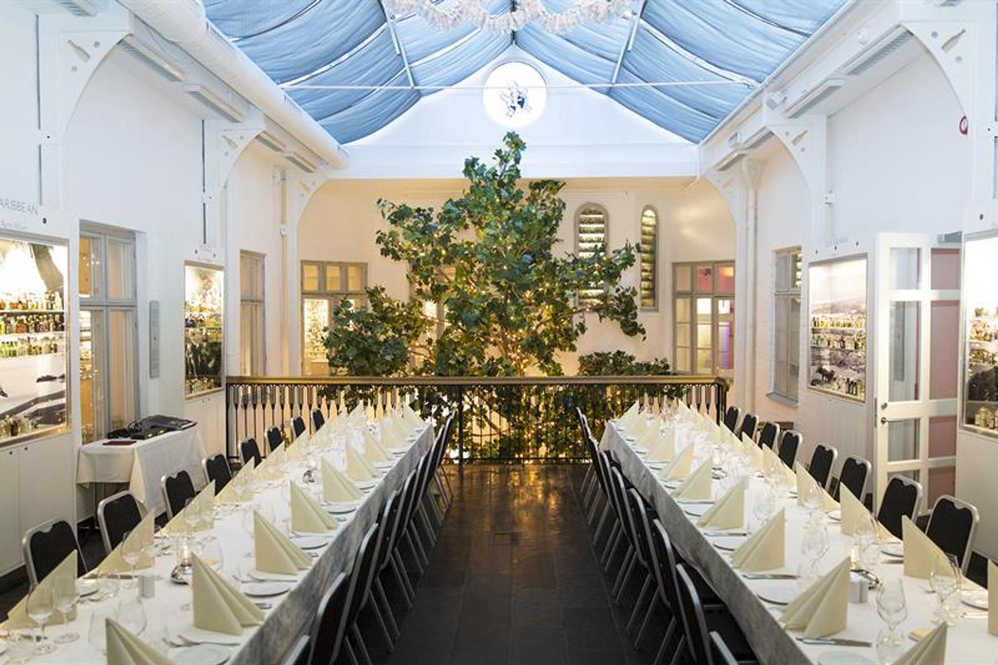 The banqueting hall with two long tables with white tablecloths and a large tree in the background