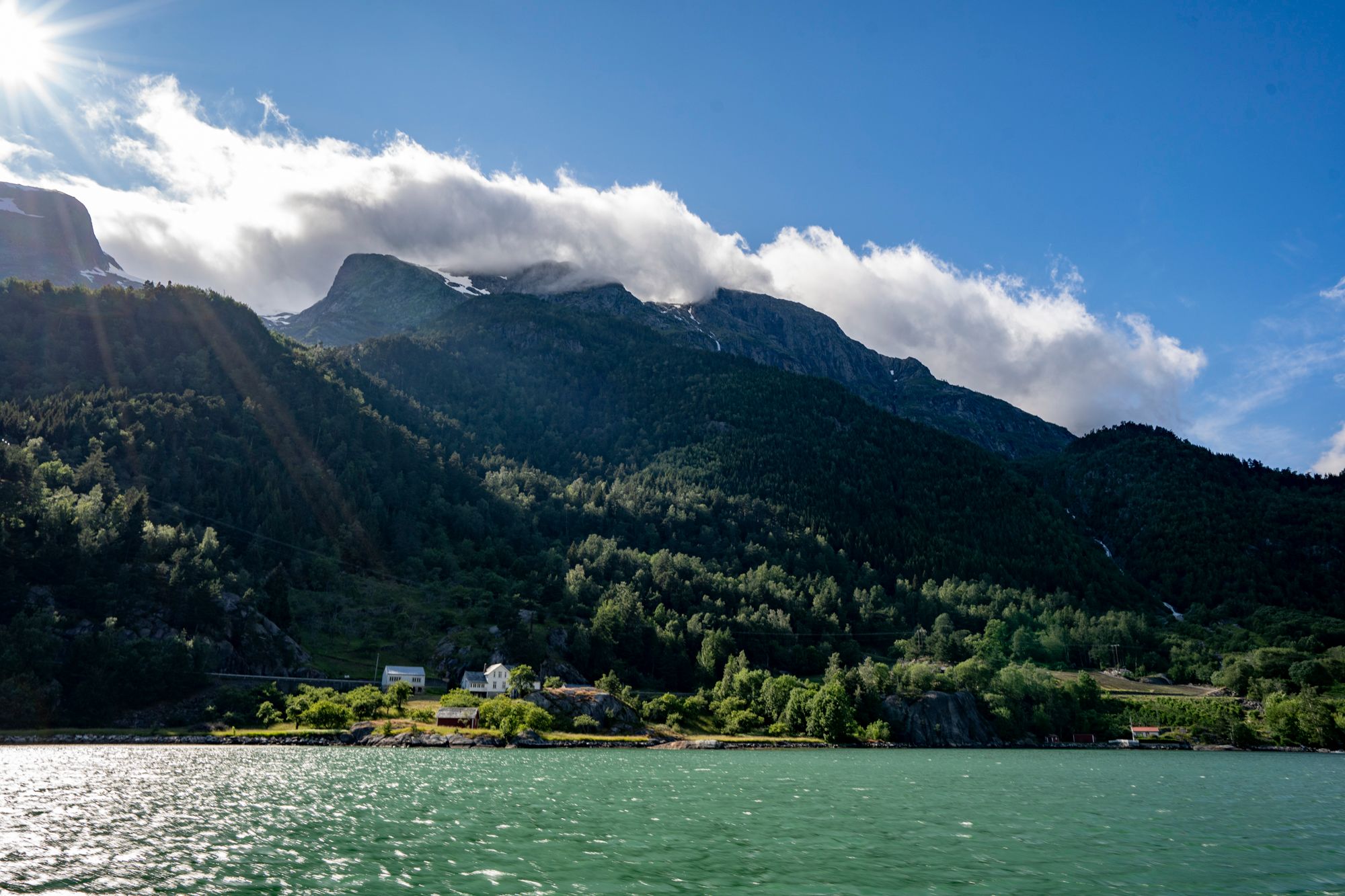 Hardangerfjorden badar i solskinn med majestetiske fjell i bakgrunnen.