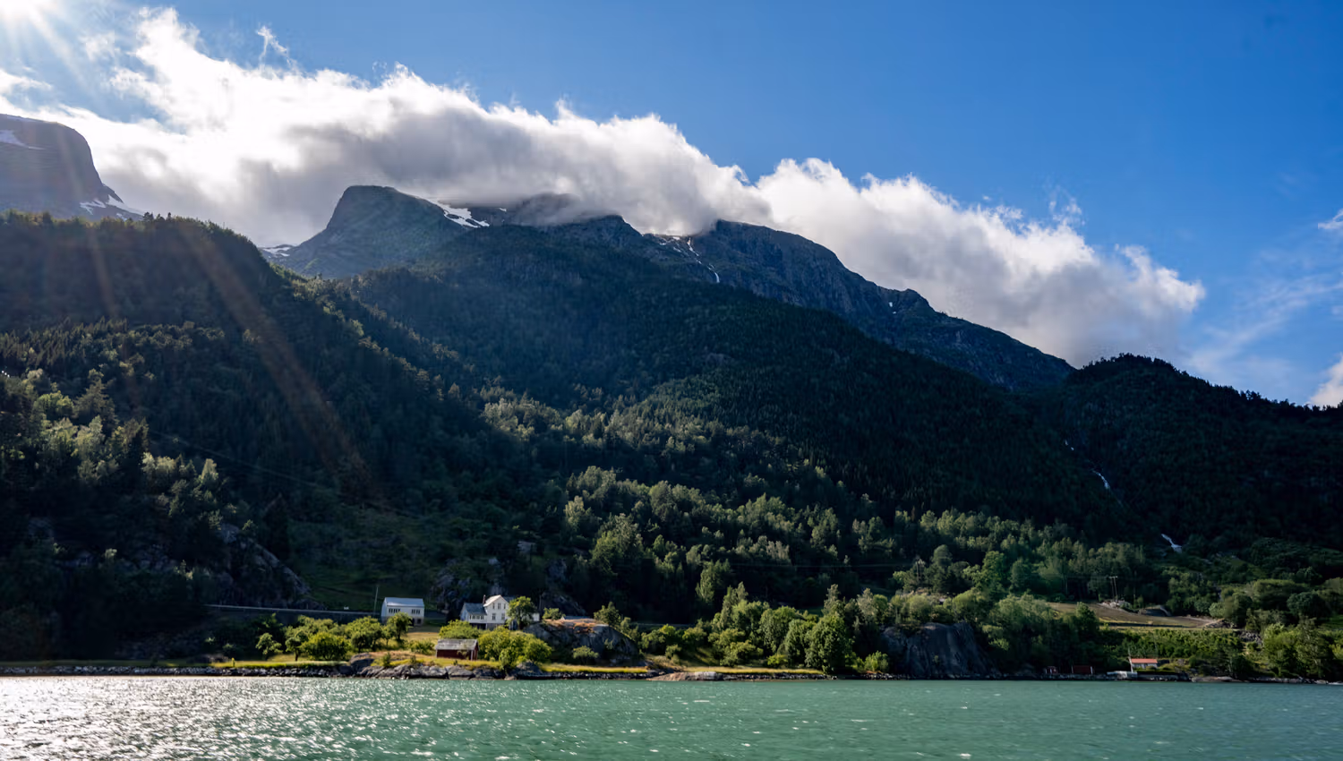 Hardangerfjorden badar i solskinn med majestetiske fjell i bakgrunnen.