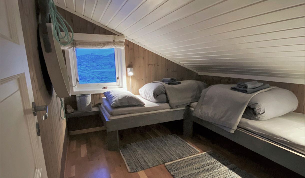 A bedrom at Nordenskiöld Lodge with two ready-made beds and a window with a tundra landscape in the background