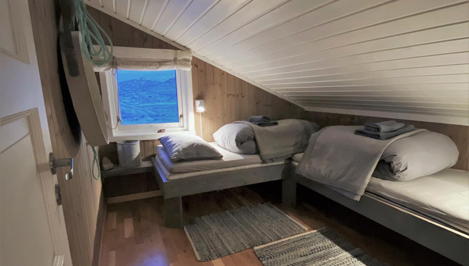 A bedrom at Nordenskiöld Lodge with two ready-made beds and a window with a tundra landscape in the background