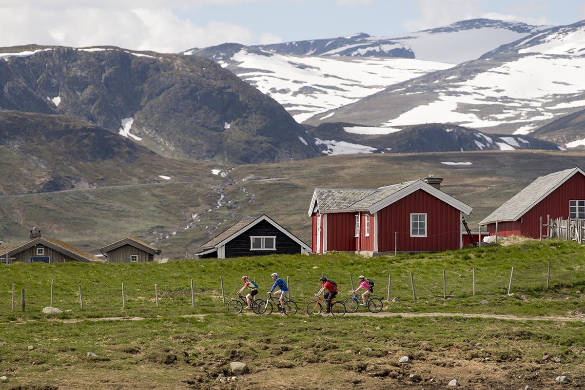 Cyclists in fron of red farm houses with a dramatic mountain scenery in the background.