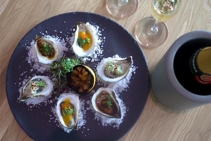 Detail of oyster on a plate with salt sprinkled around and half a lemon in the middle. Two glasses of sparkling white wine next to it.